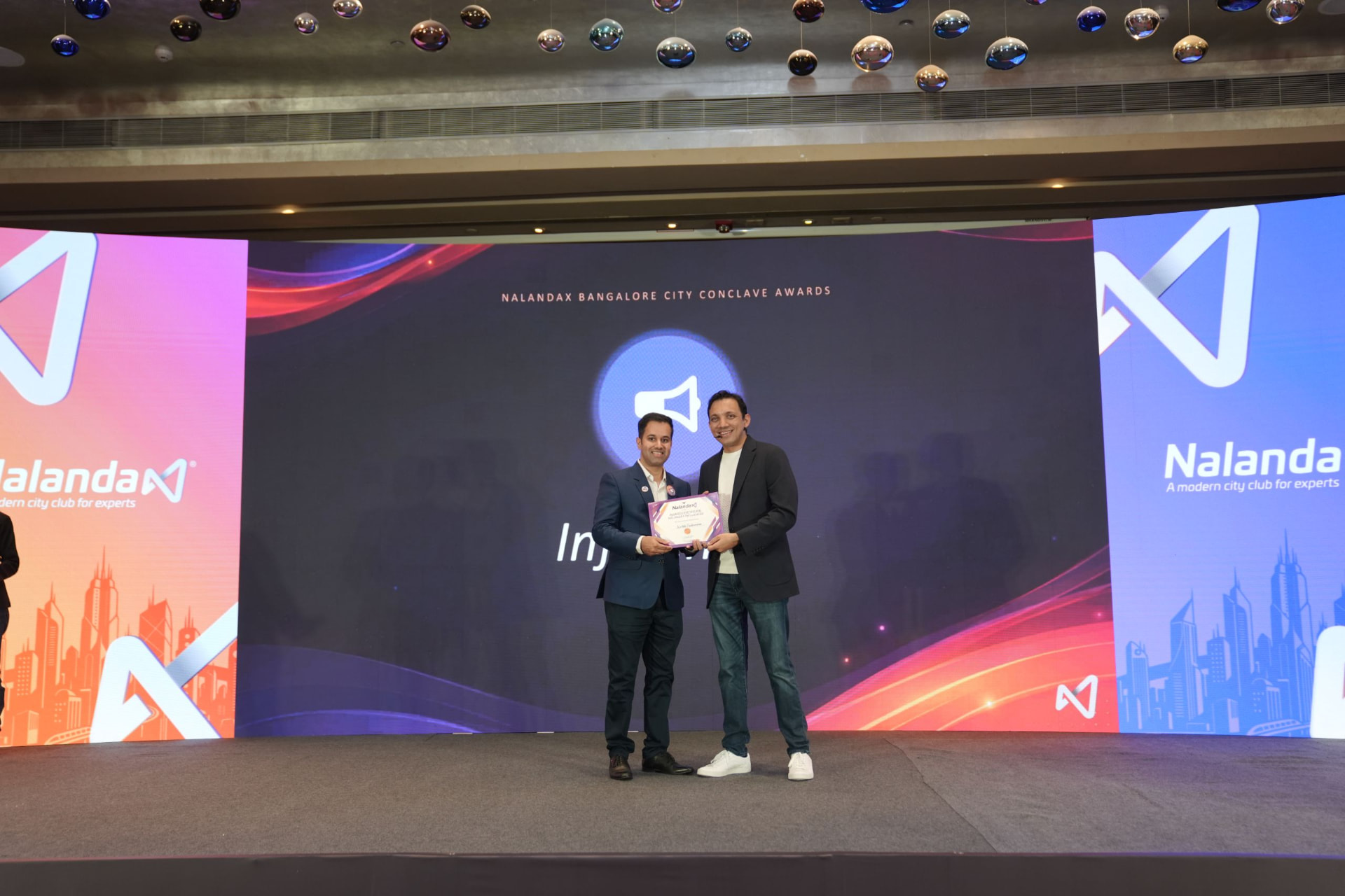 Award presentation on stage, with both people holding the certificate